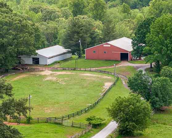 Oakside Stables sign mounted on a tree with a horse logo, surrounded by lush greenery, with red and white barn buildings visible in the background at 2205 S. Amherst Hwy, Amherst, VA 24521.